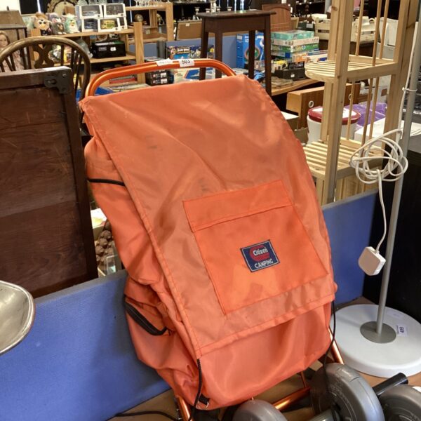 Retro orange coal scuttle with metal frame and wheels.