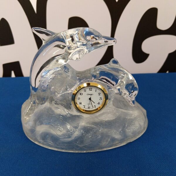 Clear crystal dolphin clock on a dark surface.