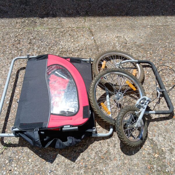 Red bike child trailer with wheels, ideal for bicycle transport.
