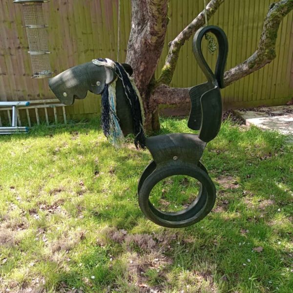 Rustic tyre horse swing in a garden setting.