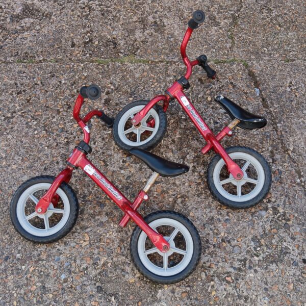 Two red child's balance bikes for learning to ride.