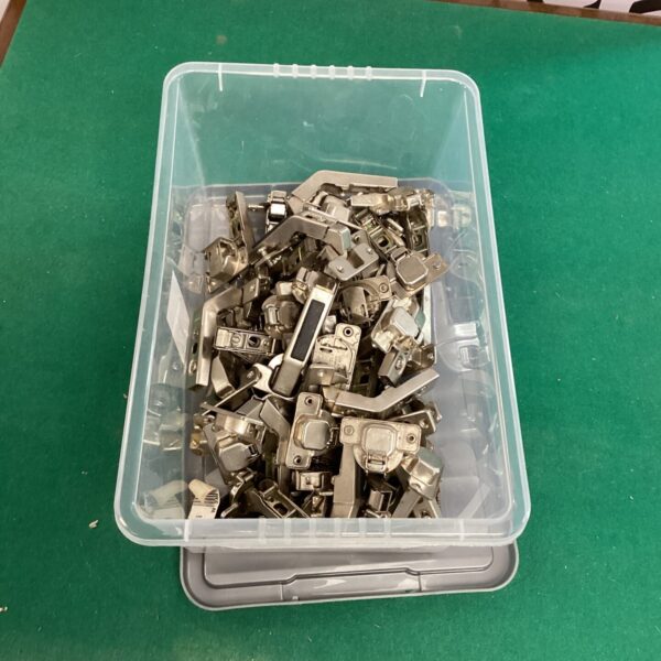 Quantity of metal kitchen cupboard hinges in a plastic container.