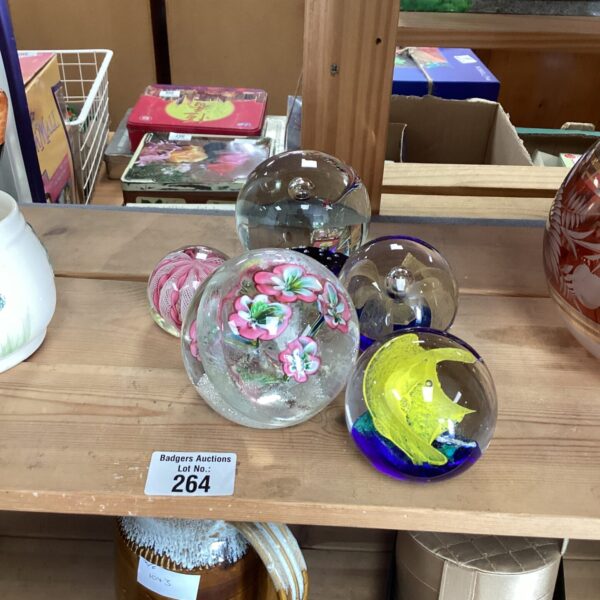 Lot of five colourful Murano glass paperweights on a wooden surface.