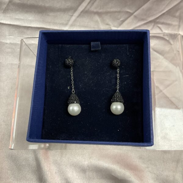 Close-up of Swarovski black crystal and pearl drop earrings in box.