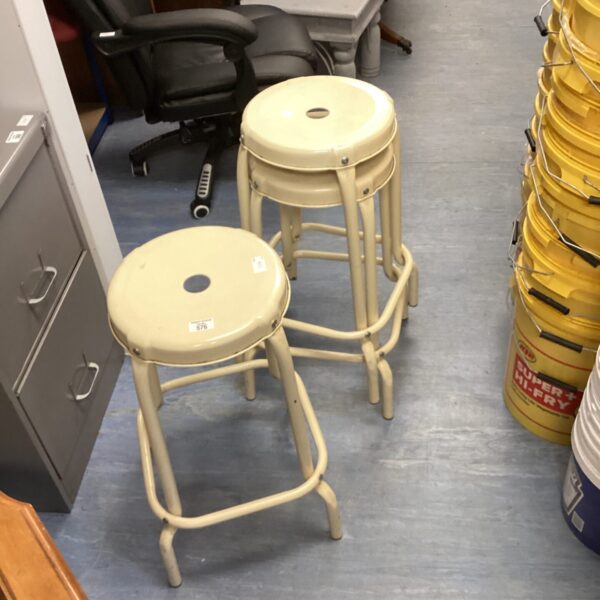Three vintage cream metal stools in a workshop setting.