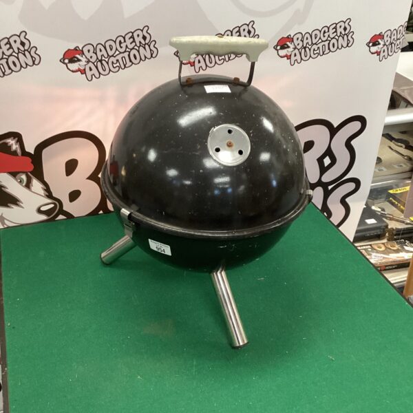 Small round BBQ grill for outdoor cooking in a garden setting.