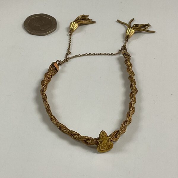 Vintage woven yellow metal bracelet with tassels and crest detail.