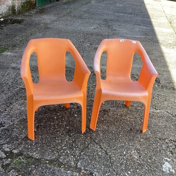 Pair of bright orange plastic garden chairs in a garden setting.