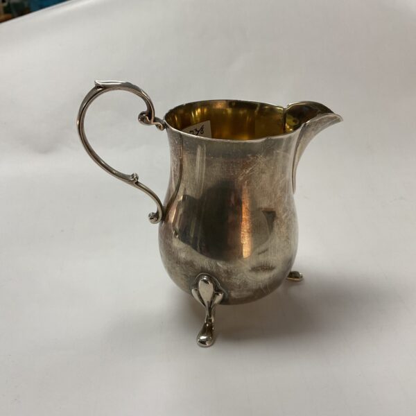 Antique silver cream jug with hallmarked detail.