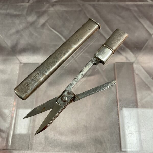 Antique silver travel scissors open, showing serrated blades.
