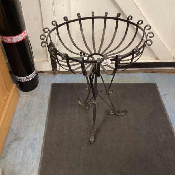 Vintage metal flower basket on tripod stand for garden display.
