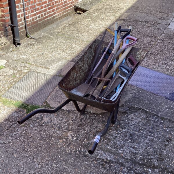 Rusted vintage wheelbarrow filled with gardening tools in a garden setting.