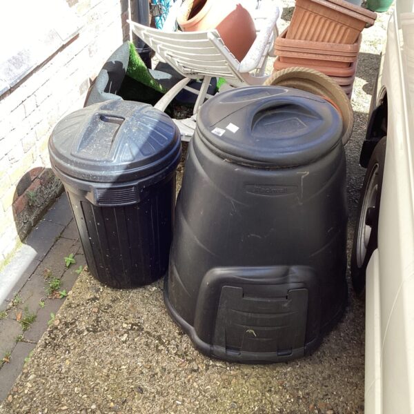 Dark plastic compost bin and dustbin in a garden setting.