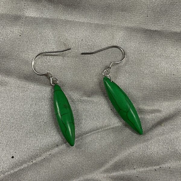 Close-up of green stone drop earrings on a neutral background.