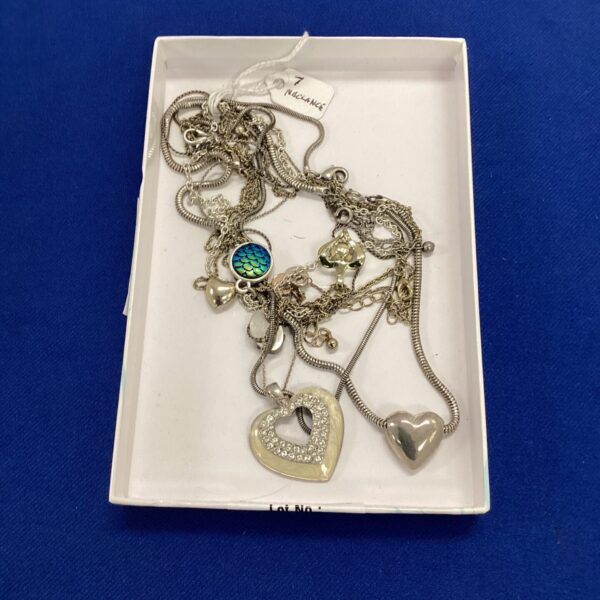 Tray of seven white metal necklaces with varied pendants.