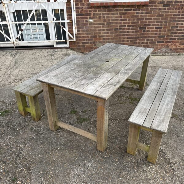 Weathered teak garden table with two benches in a garden setting.