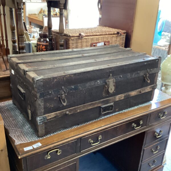 Antique steamer trunk stacked on a dark wood desk.