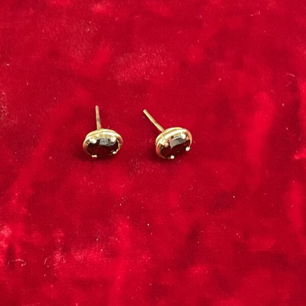 Close-up of 9ct gold garnet stud earrings with red gemstones.