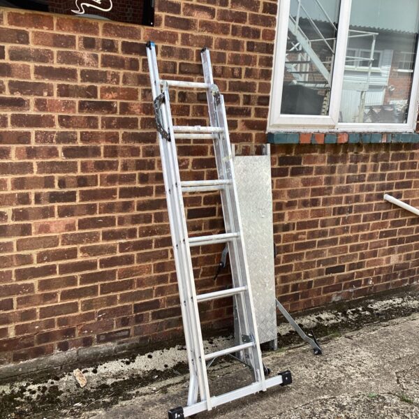 Silver aluminium folding platform ladder against a brick wall.