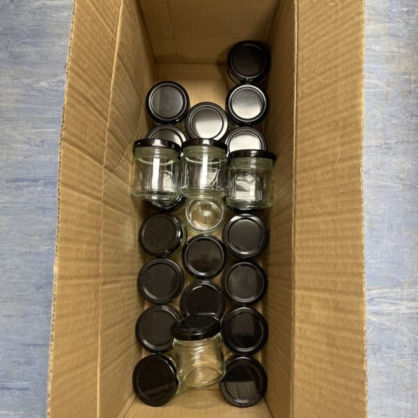Box of miniature glass preserve pots with black lids.