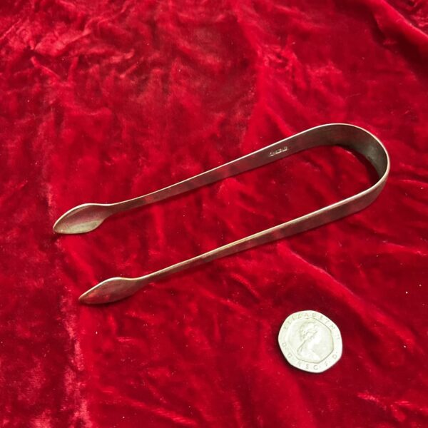 Antique Georgian silver sugar tongs on a red background.
