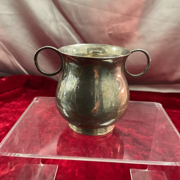 Antique silver twin handled bowl on a red display stand.
