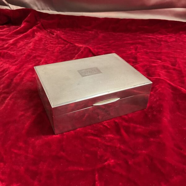 Silver cigarette box on a red velvet background, engraved with inscription.