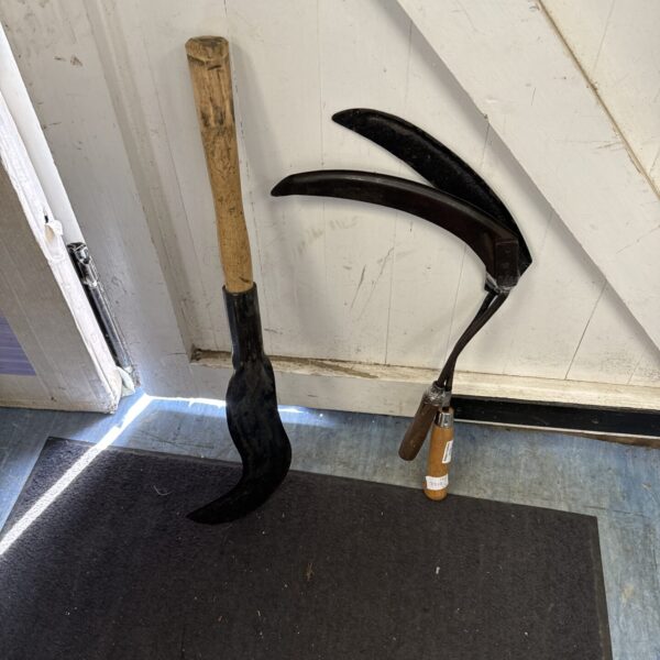 Vintage hand scythe with curved blade and wooden shaft.