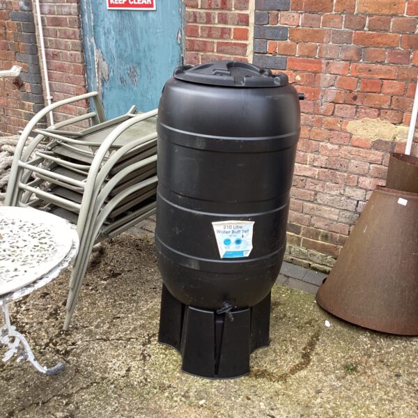 Black 210 litre water butt with tap and stand in a garden.