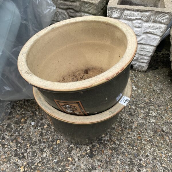 Two large green terracotta plant pots in a garden setting.