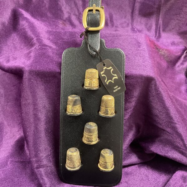 Close-up of six antique sterling silver thimbles on a leather strap.