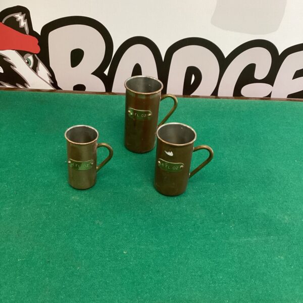 Three vintage copper measuring jugs displayed together.