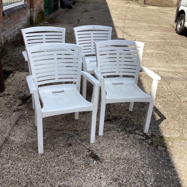 Set of four white plastic garden chairs in a garden setting.