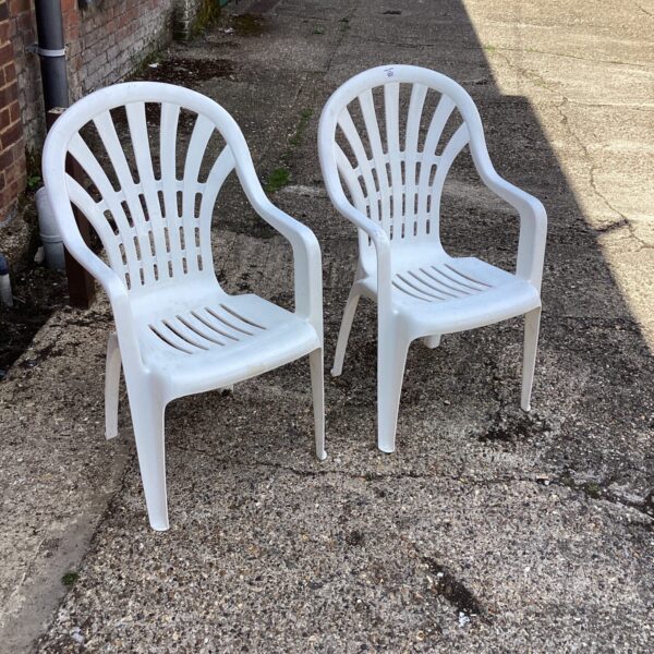 Two white plastic garden chairs in a garden setting.