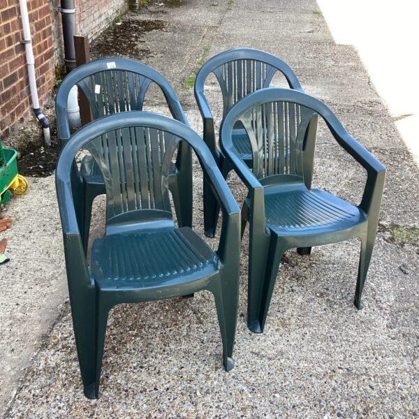 Set of four green plastic garden chairs in a garden setting.