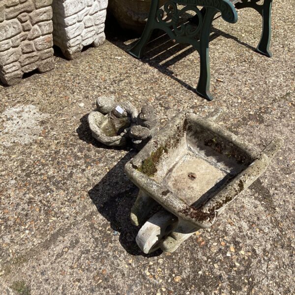 Weathered stone wheelbarrow bird bath in a garden setting.