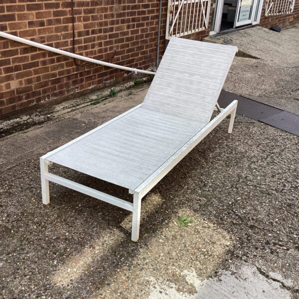 White sun lounger in a garden setting, perfect for outdoor relaxation.