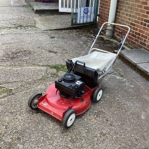 Side view of a used Toro professional lawn mower in a garden setting.