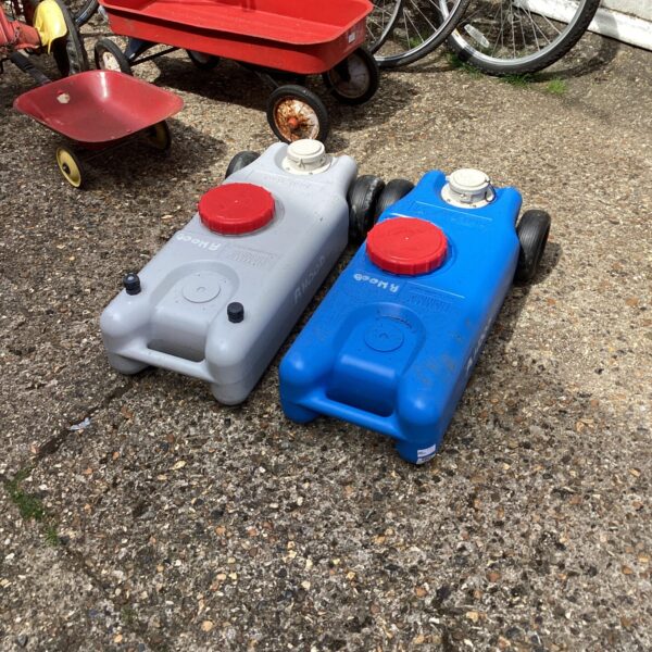 Two vintage roll tank water carriers in a garden setting.