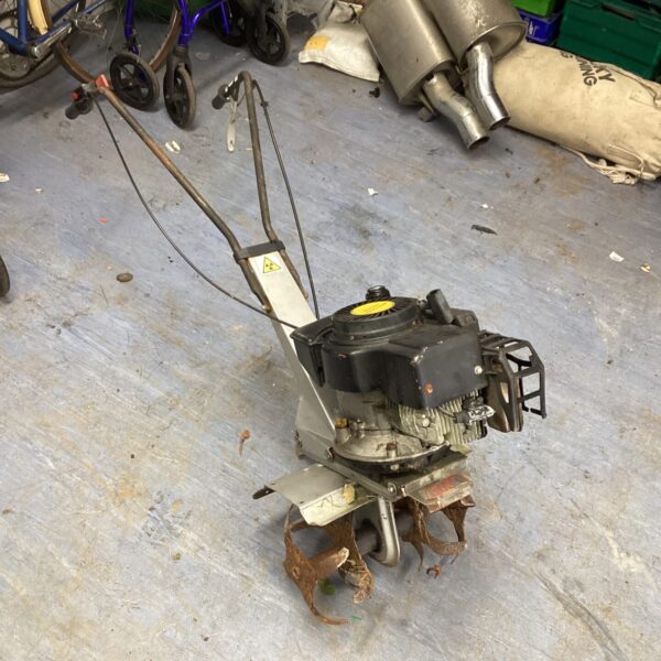 Side view of a used petrol rotovator for garden soil cultivation.