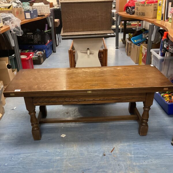 Vintage oak swivel top coffee table in a cluttered room.