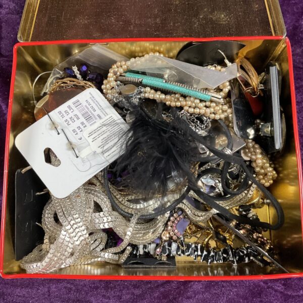Tin filled with assorted costume jewellery and beads.