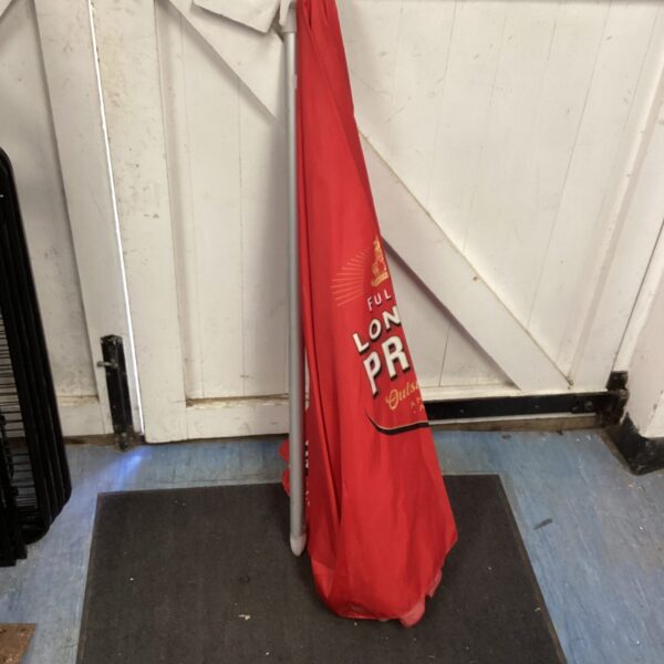 Red London Pride branded patio umbrella in a garden setting.