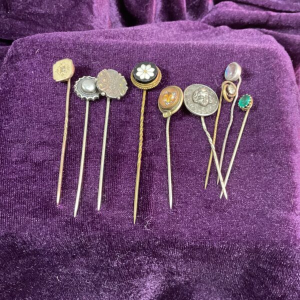 Close-up of nine vintage stick pins on a purple velvet background.