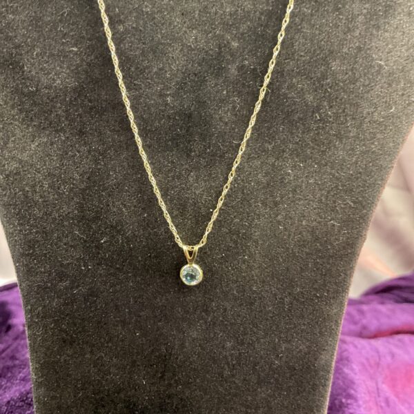 Close-up of 9ct gold blue topaz pendant on a display stand.