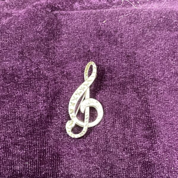 Close-up of a silver treble clef brooch with intricate detailing.