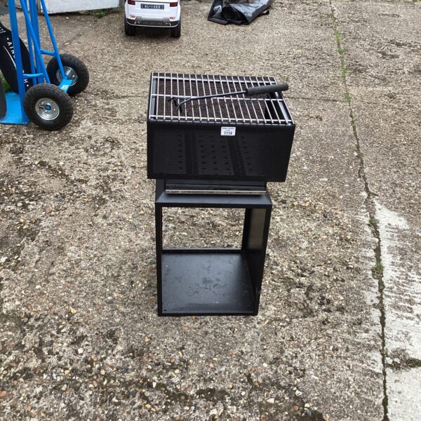 Black metal fire basket for outdoor cooking in a garden setting.