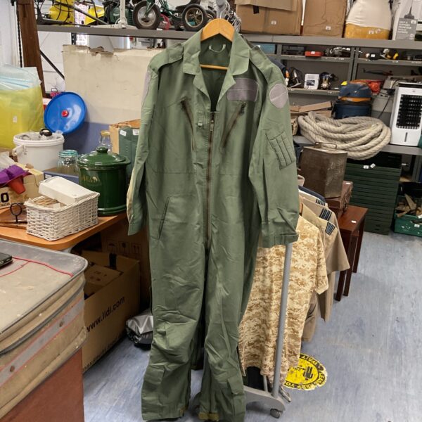 Green British Nomex flying suit hanging in a cluttered workshop.