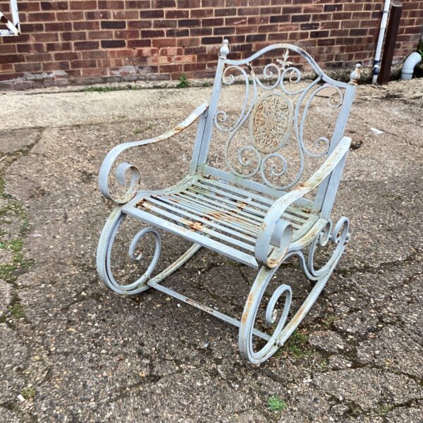Weathered vintage metal garden rocking chair with scrolling details.