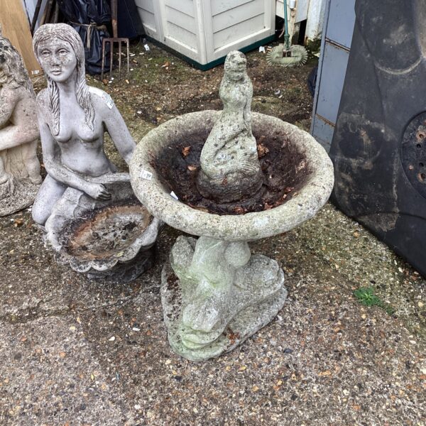 Vintage stone bird bath with sculpted bird and serpent design in garden.